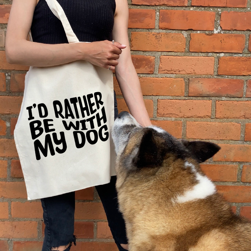a woman holding a tote bag that says i'd rather be with my dog and standing by a dog