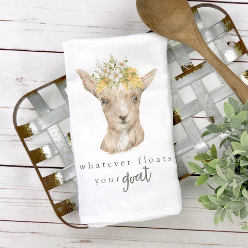 a dish towel with a goat wearing a flower crown with the words whatever floats  your goat on it