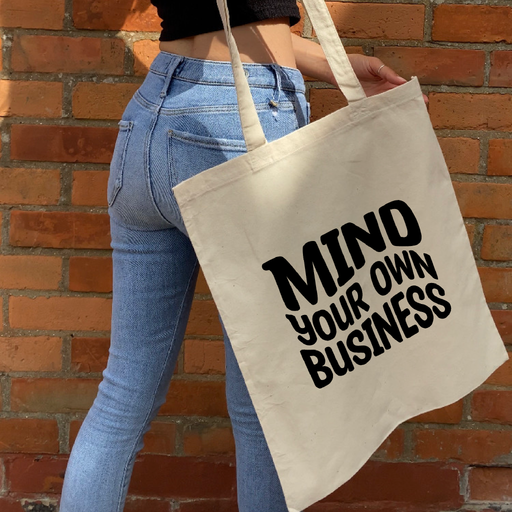 a woman holding a tote bag with mind your own business on it