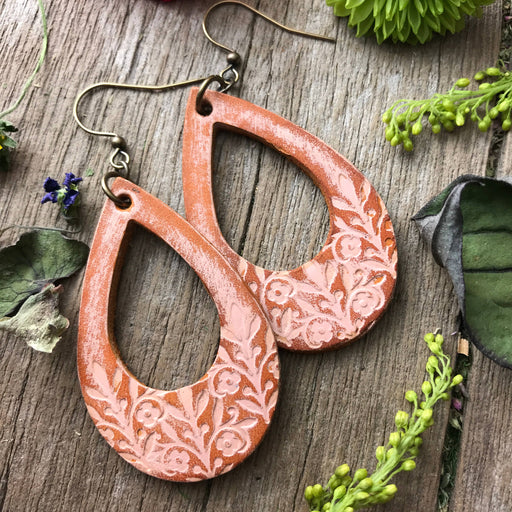a pair of leather earrings sitting on top of a wooden table