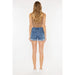 the back of a woman wearing a tan top and denim shorts