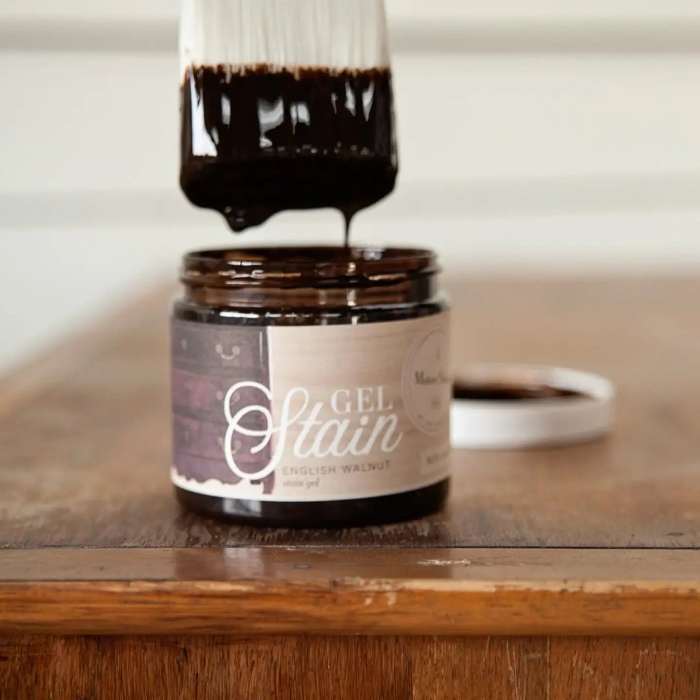 a close up of a jar of stain on a table with paint brush dipping into it