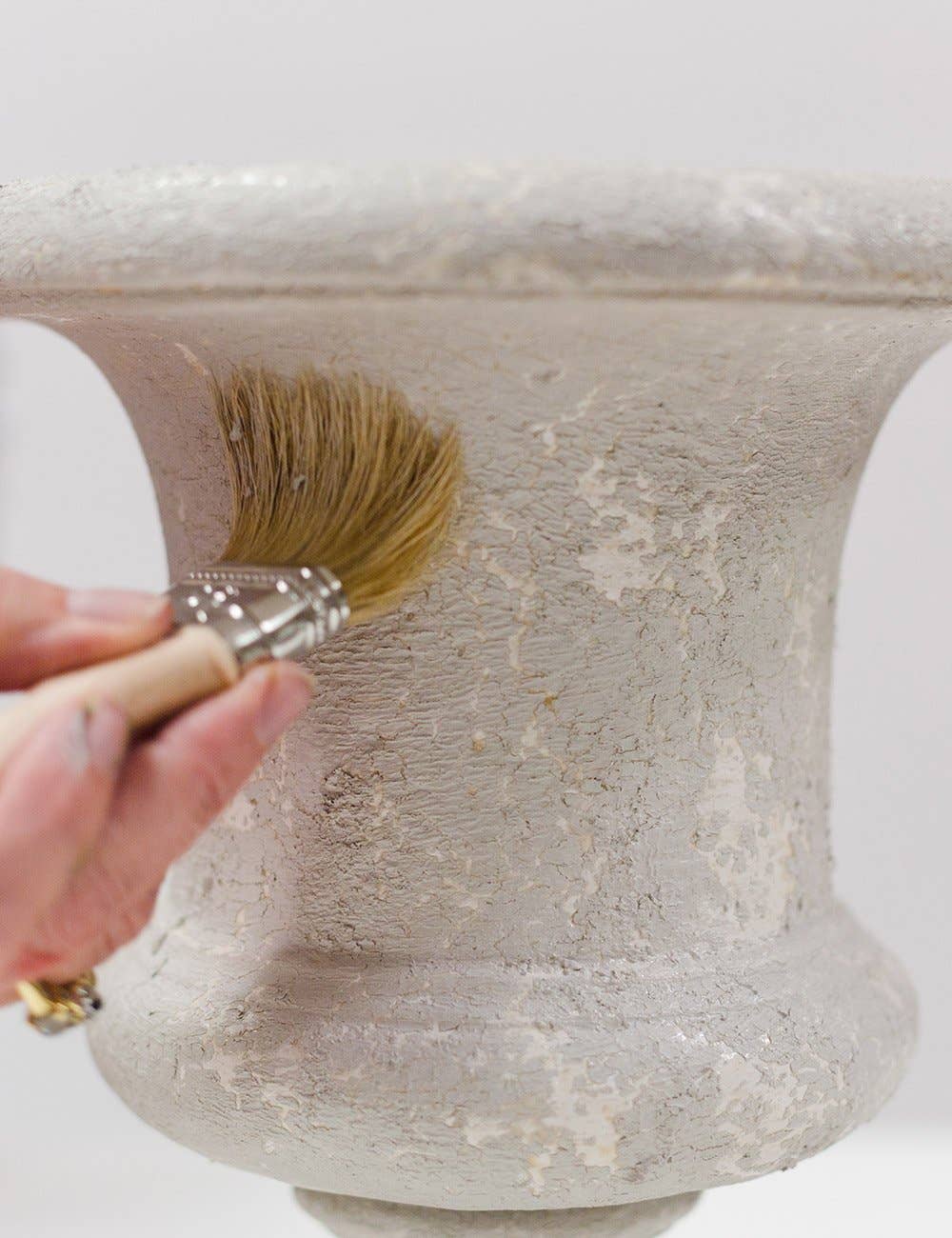 a vase with a paintbrush applying a cracked patina