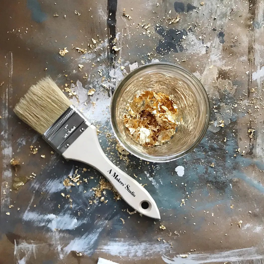 a paintbrush and a bowl of gold flakes