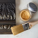 a paintbrush and a can of gold paint sitting on a table