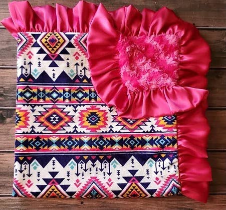 a pink ruffle on top of a pink aztec print baby blanket