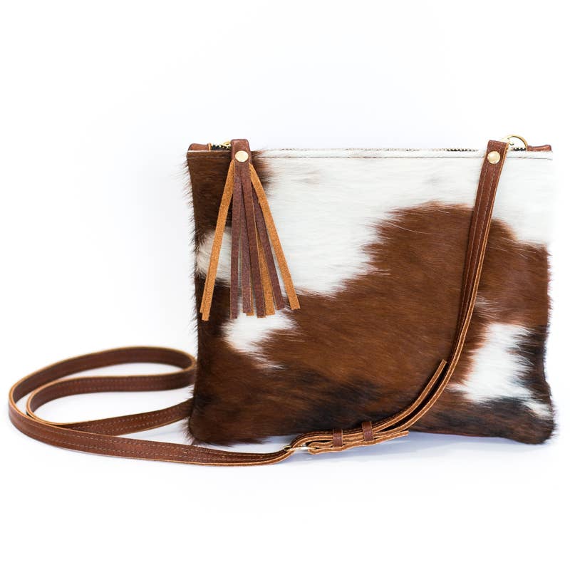 a brown and white cowhide crossbody purse with a tassel