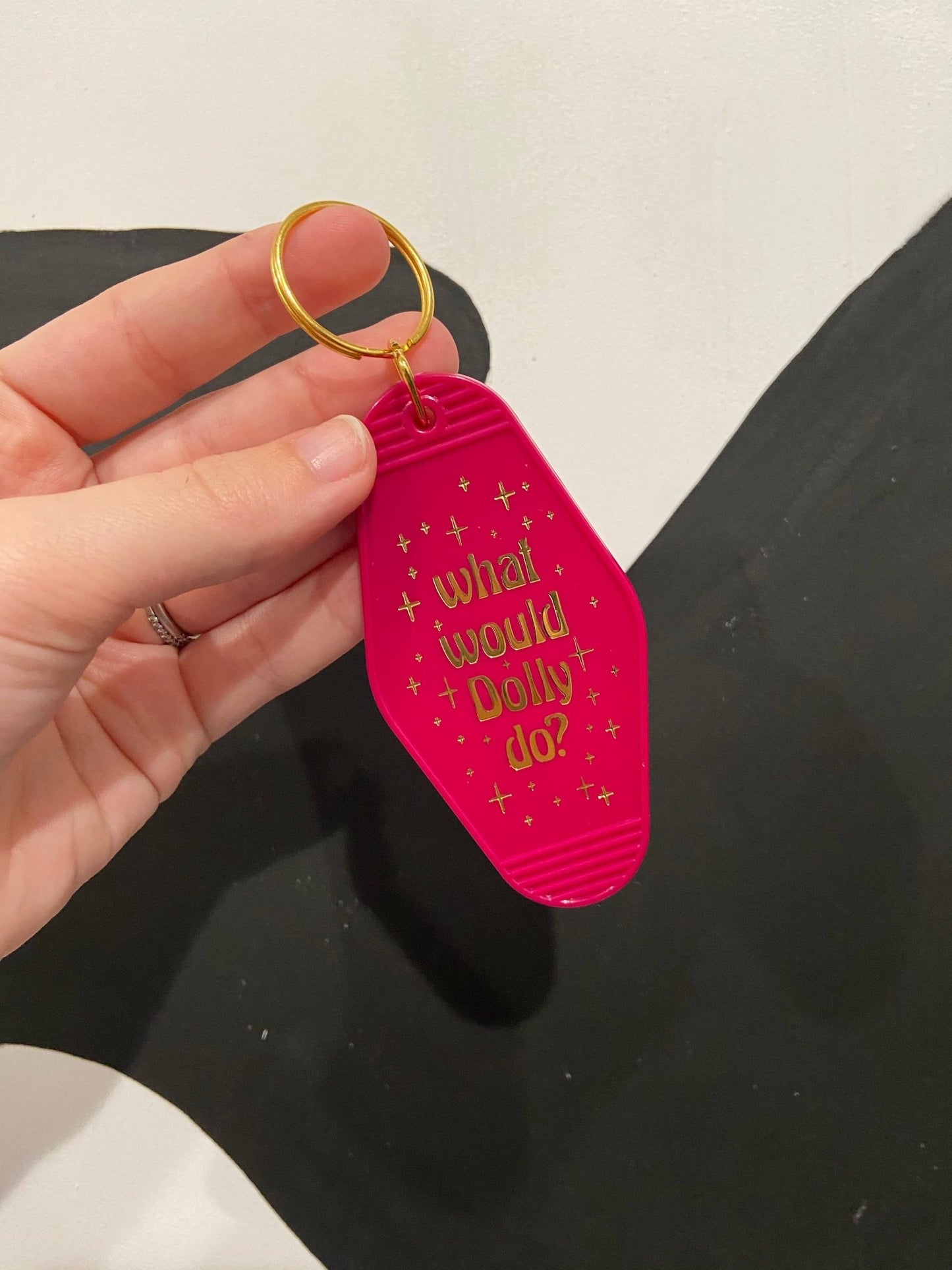 a hand holding a fuschia pink keychain that says what would Dolly do?