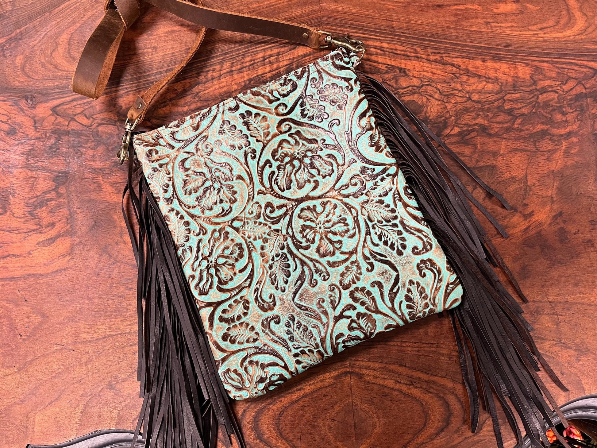 a turquoise and brown tooled leather crossbody purse with fringe hanging from it