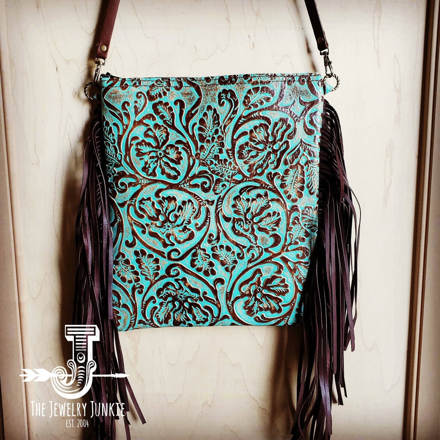 a turquoise and brown tooled leather crossbody purse with fringe hanging from it