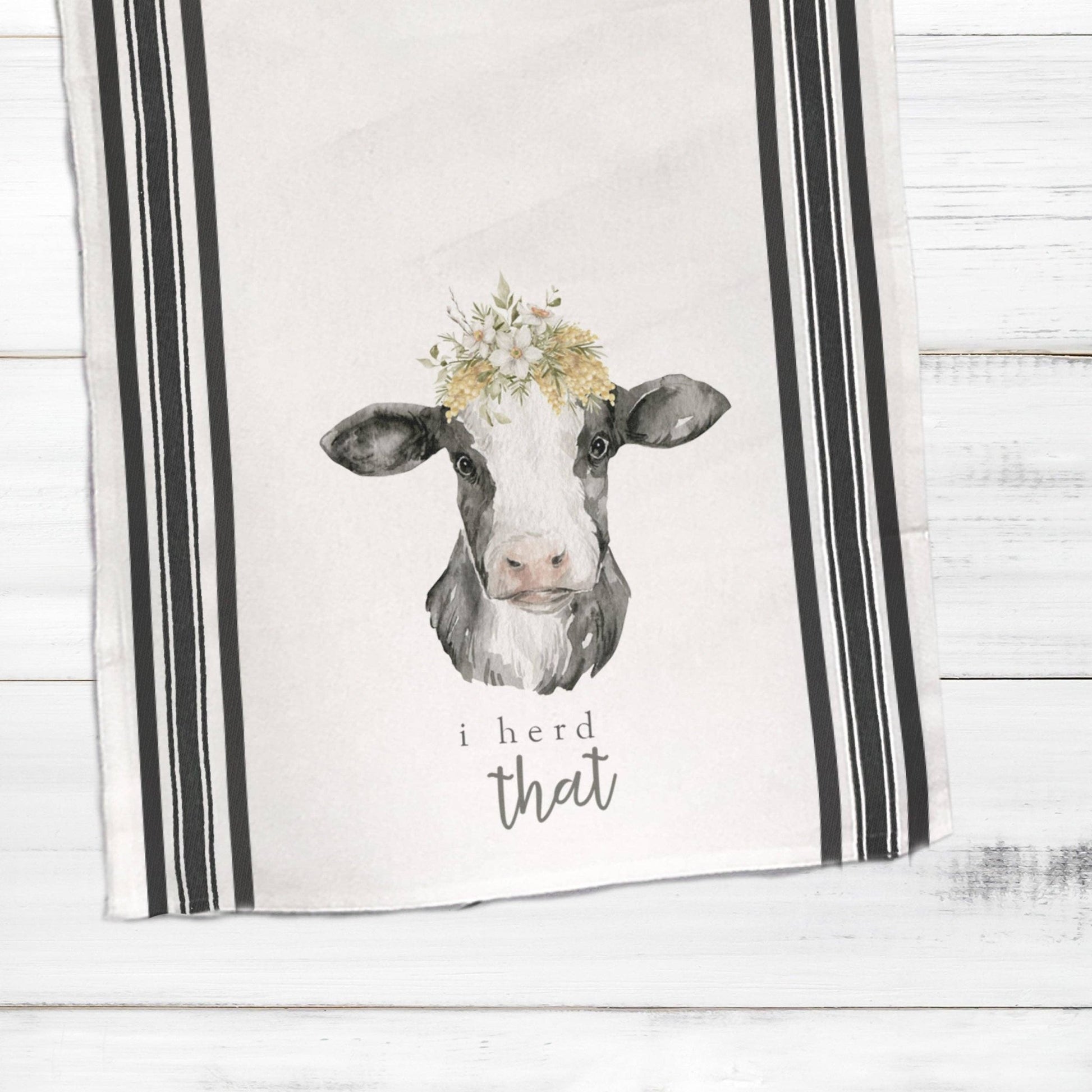 a tea towel with a picture of a cow wearing a flower crown and an inscription that says I herd that