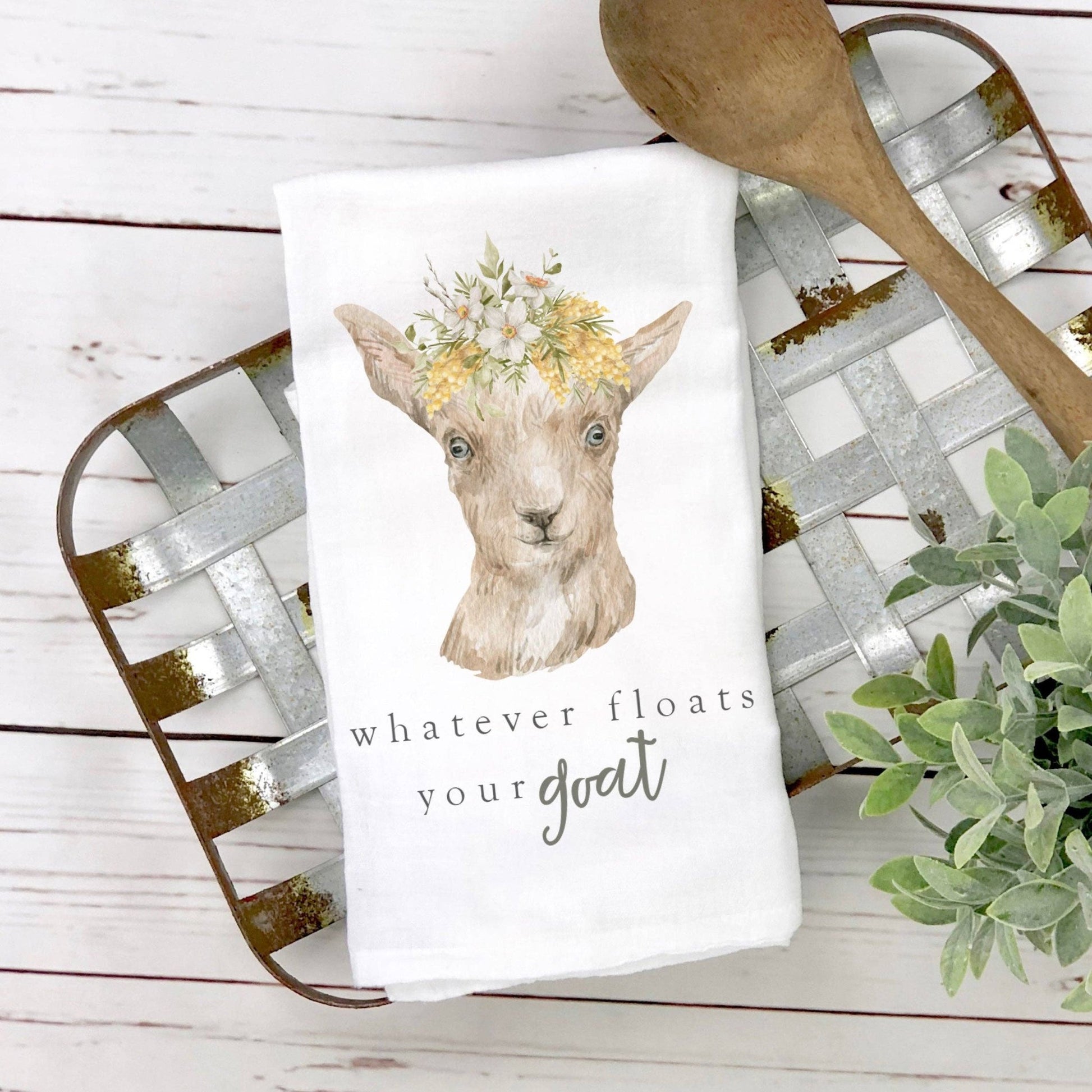 a dish towel with a goat wearing a flower crown with the words whatever floats  your goat on it