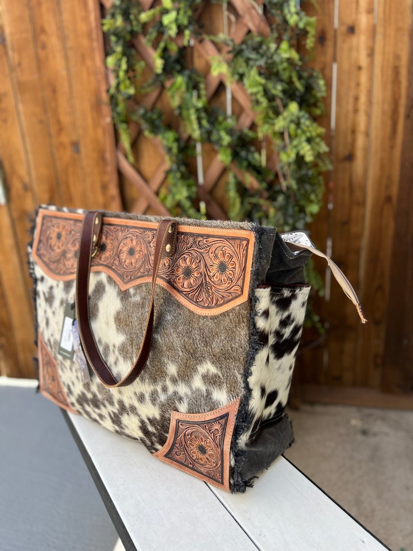 a black and white cowhide and tooled leather weekender bag sitting on top of a table