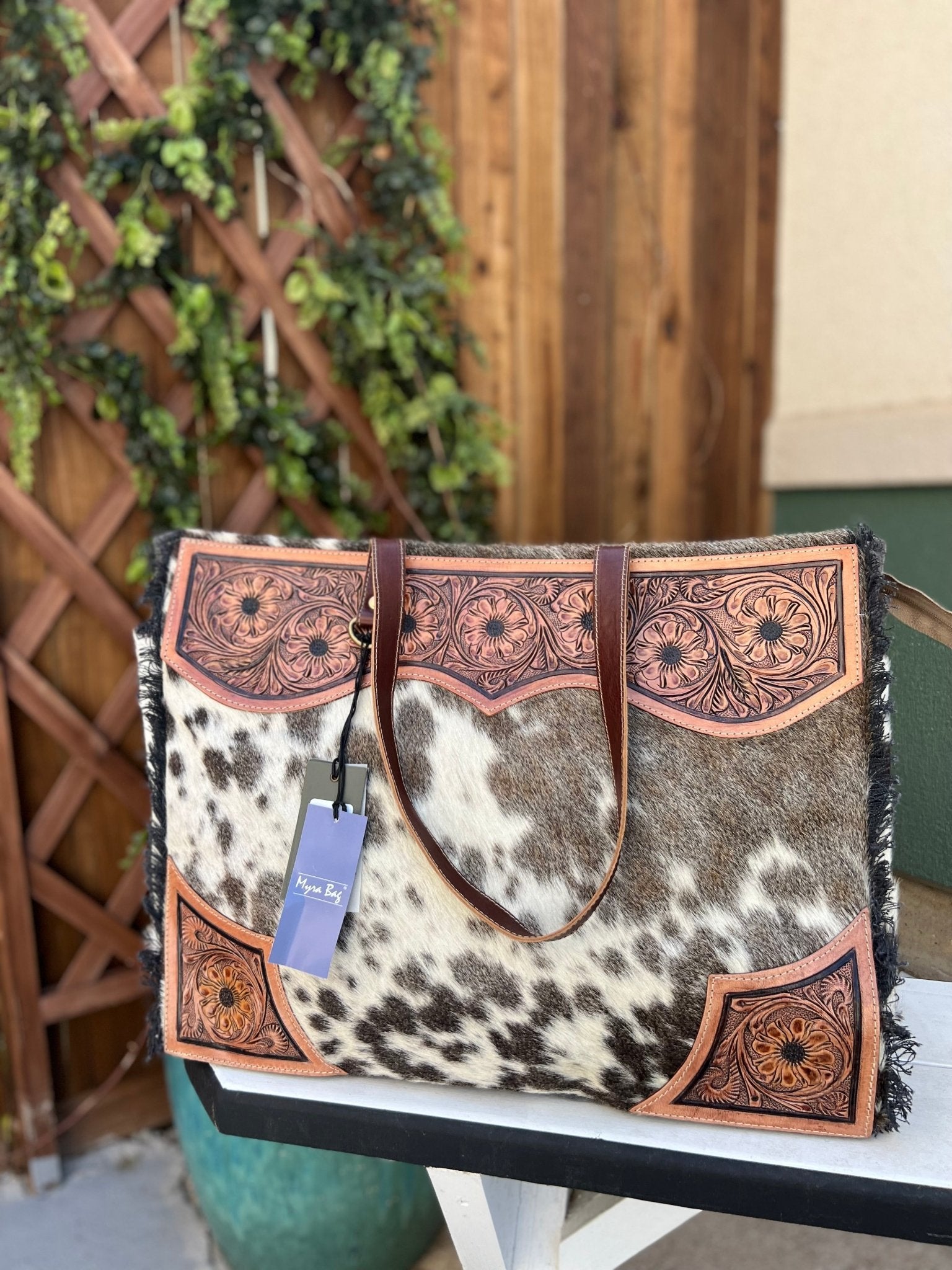 a black and white cowhide and tooled leather weekender bag