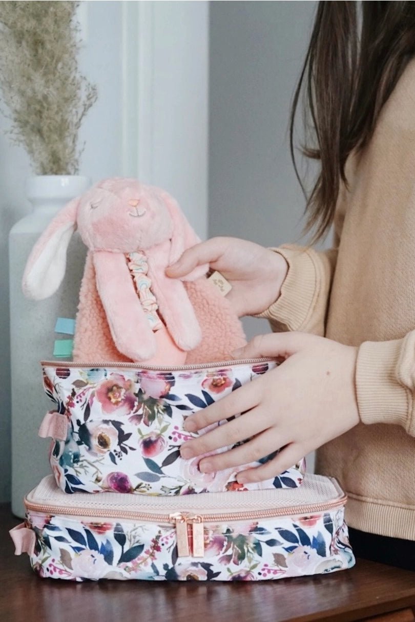 a woman holding a pink stuffed animal on top of a suitcase