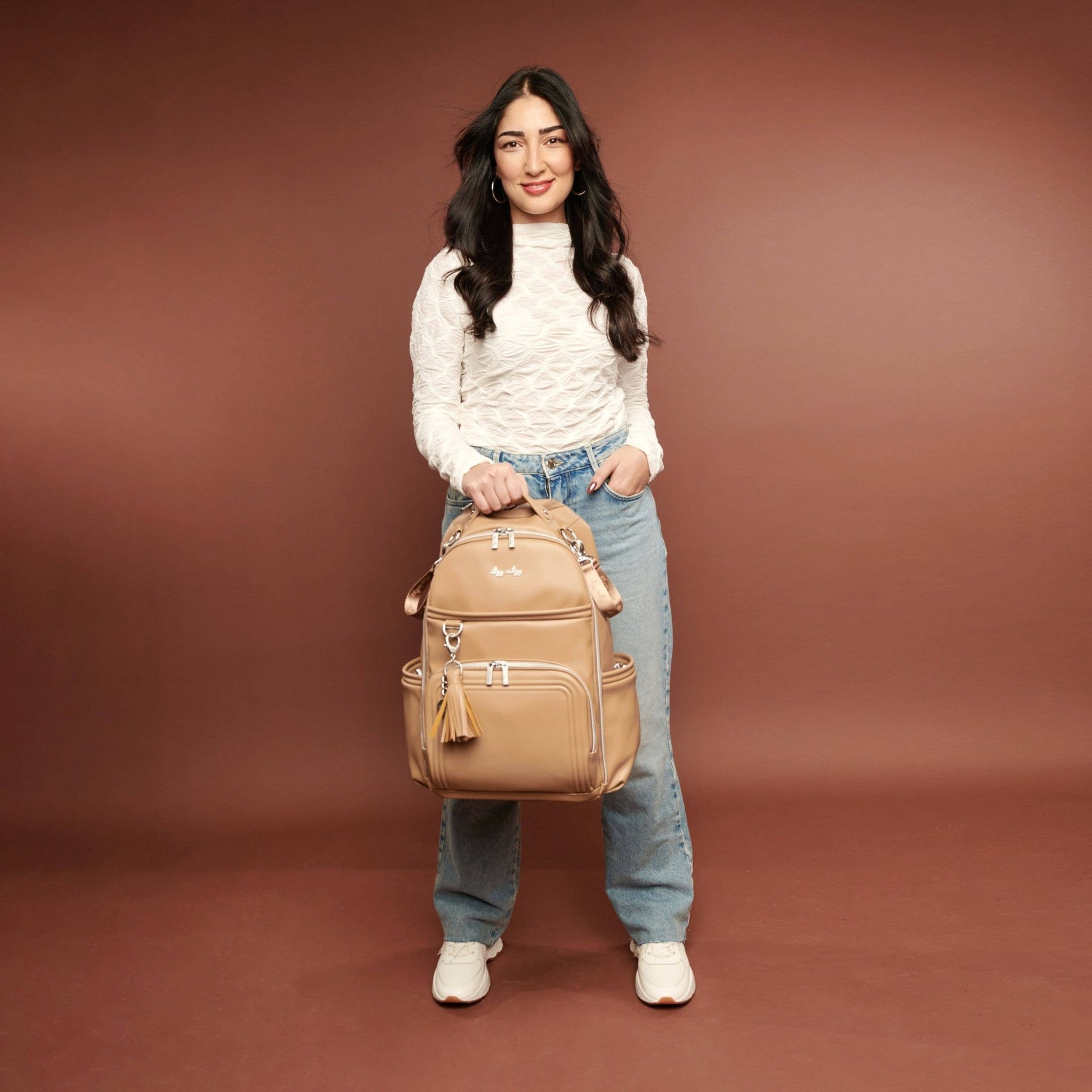 a woman is holding a brown backpack and smiling