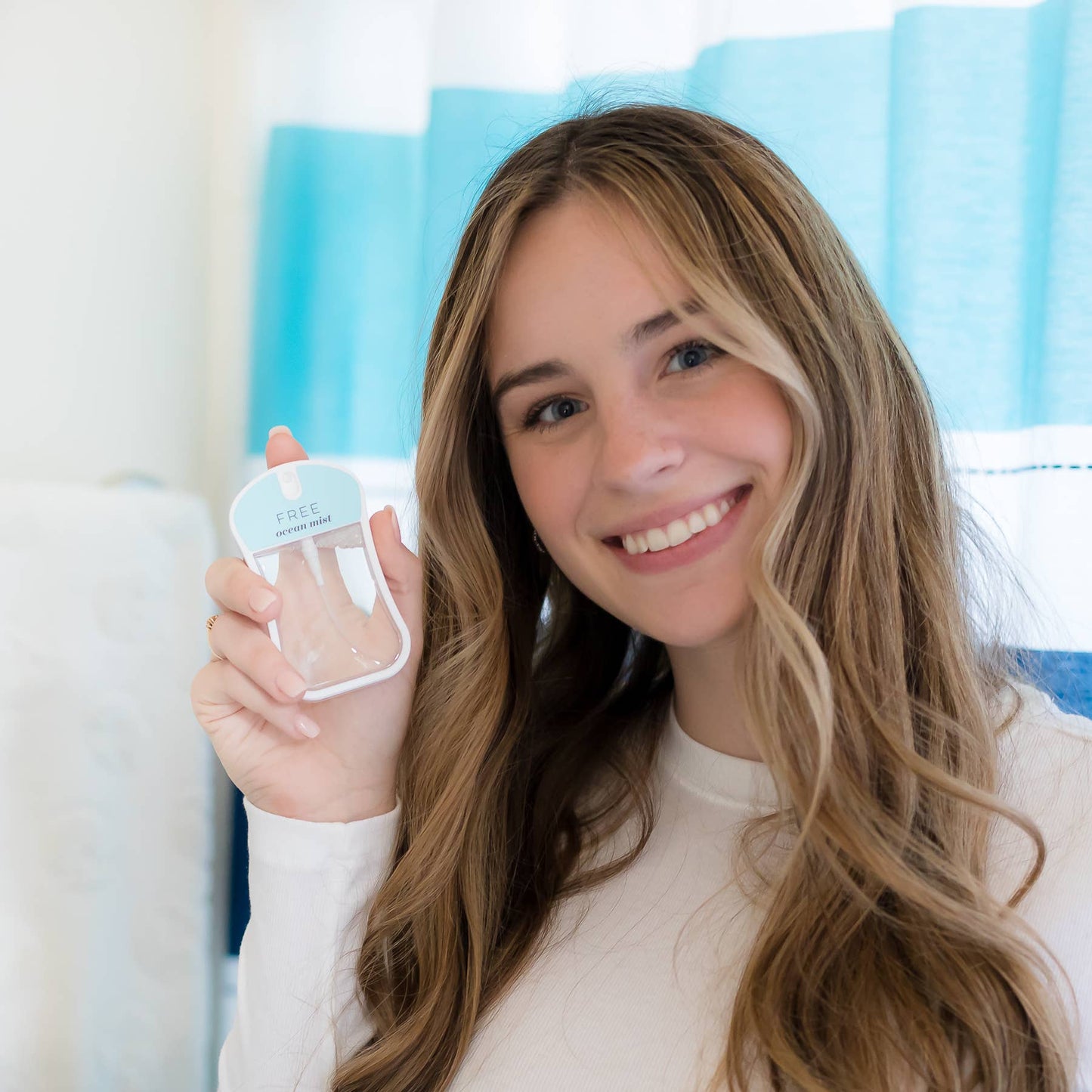 a woman holding up a clear plastic body mist container