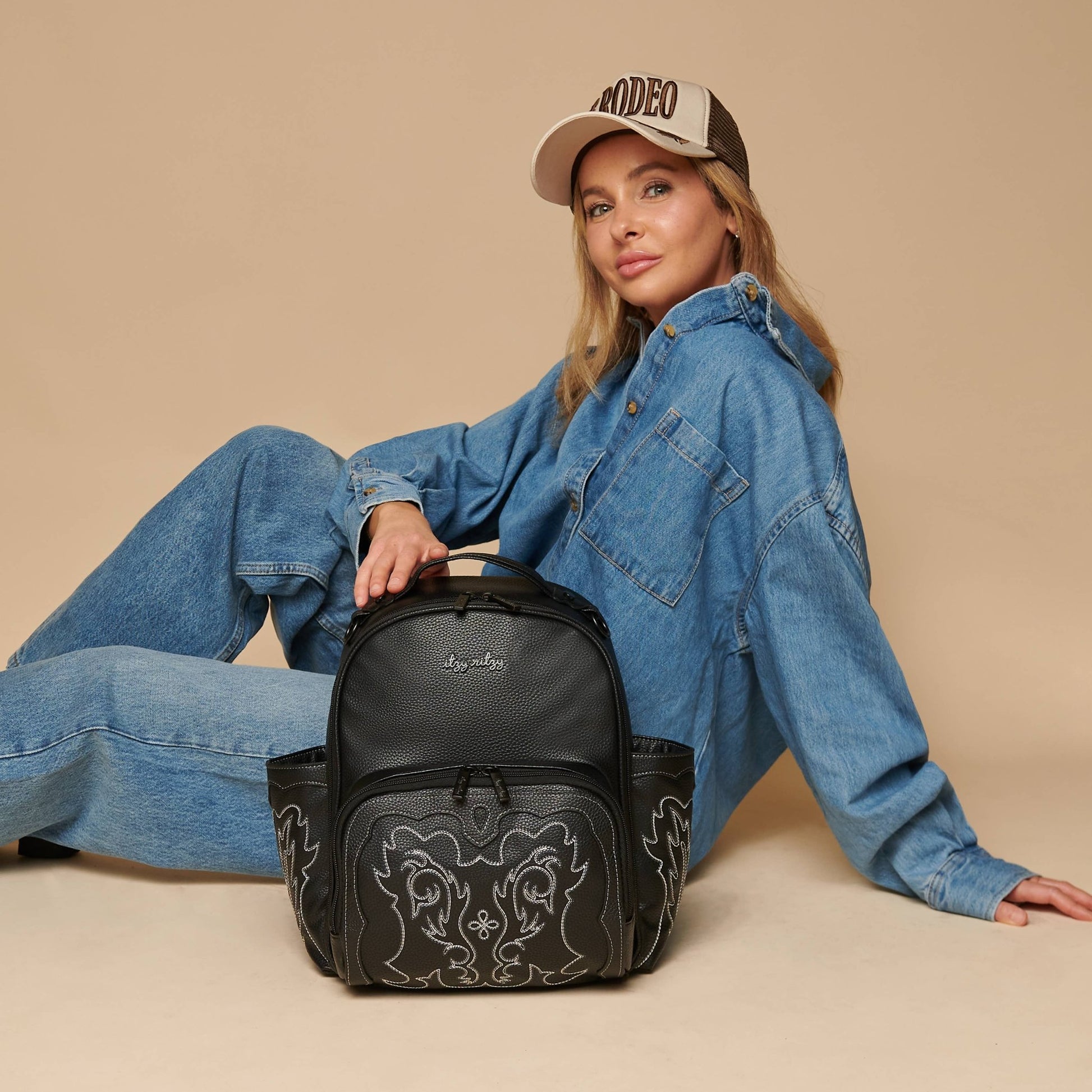 a woman sitting on the floor with a Itzy Ritzy Nash Outlaw Itzy Mini Plus