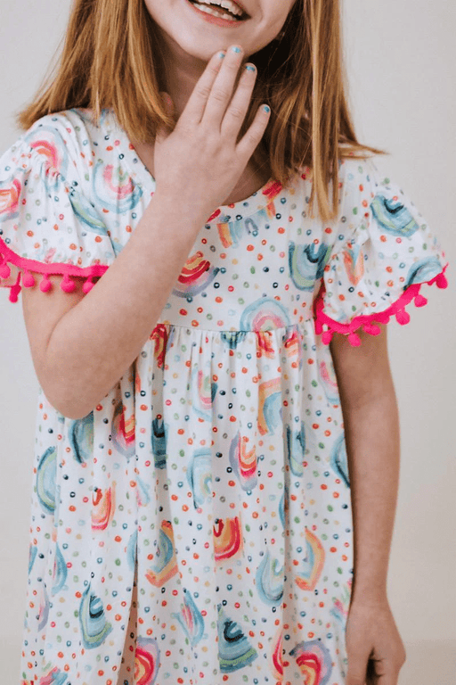 a little girl in a pom pom dress with rainbows on it