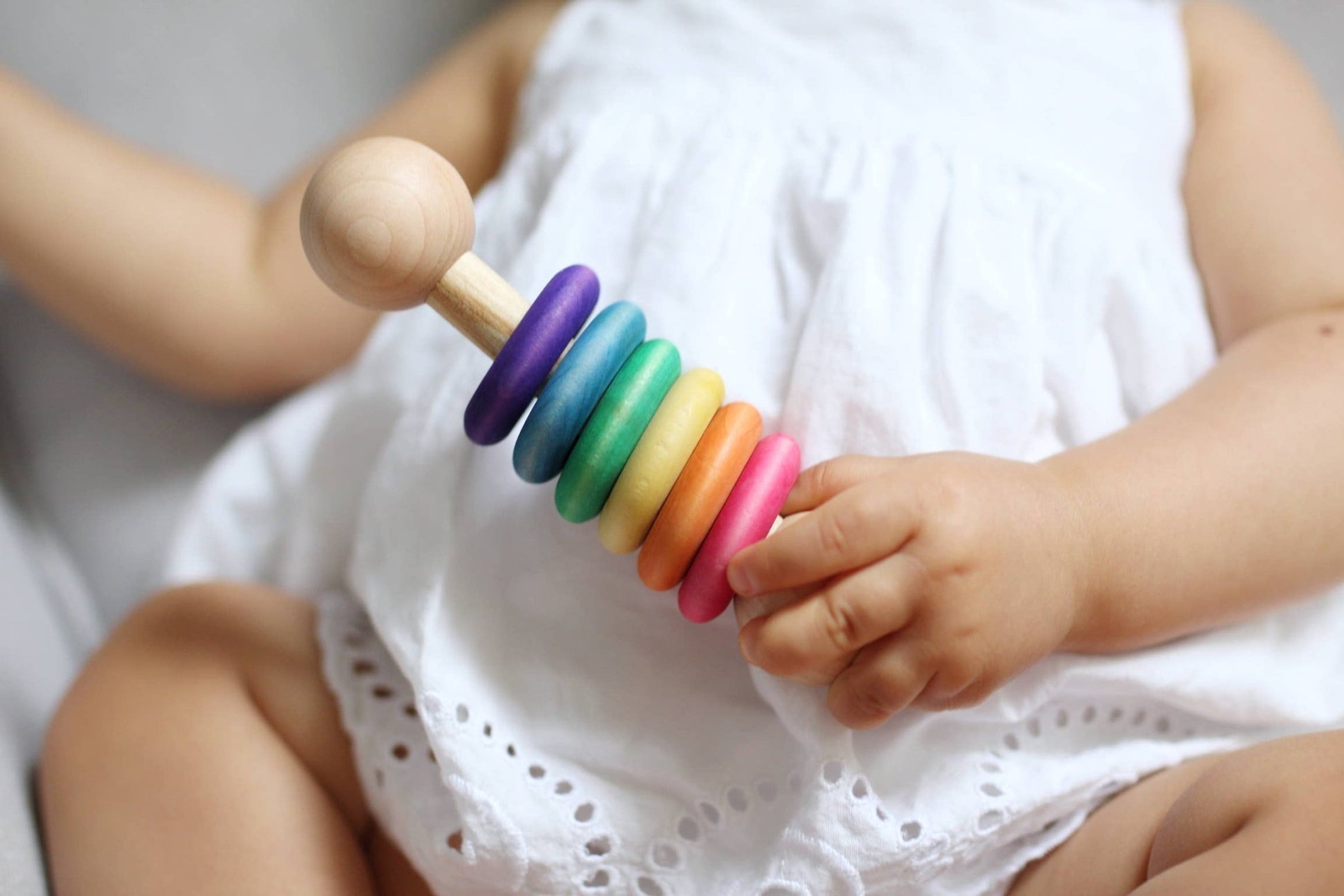 a baby holding a colorful rainbow colored rattle