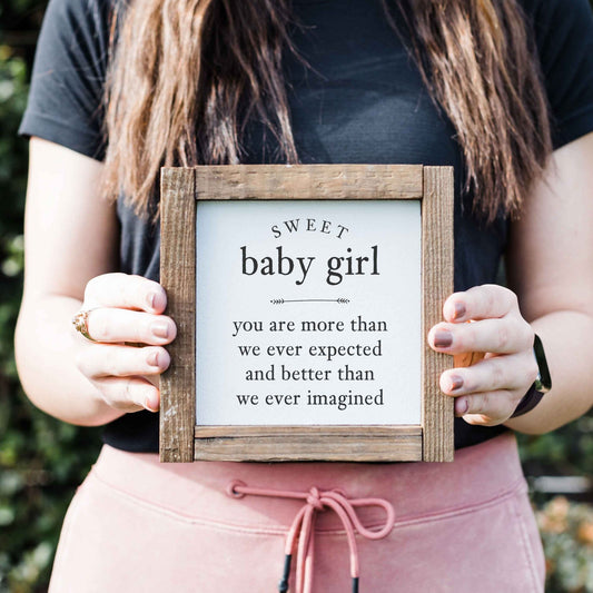 a woman holding a sign that says, sweet baby girl you are more than we ever expected and better than we ever imagined