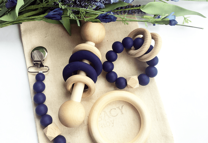 a teething Rattle Gift Set out of wood and Navy Blue silicone sitting on a muslin bag and a white background