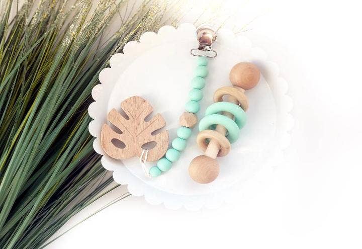 a wooden teething rattle and beaded teether on a plate next to a plant