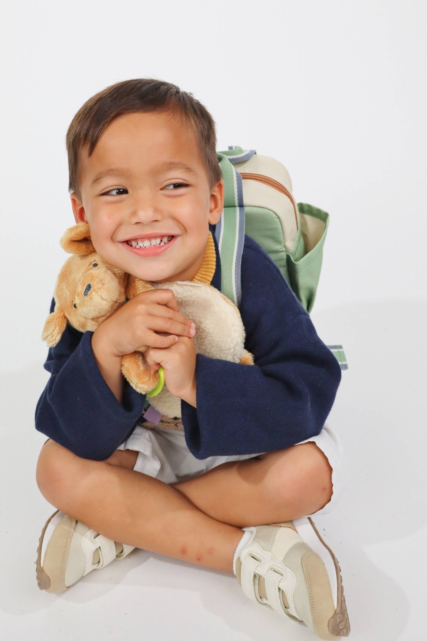 a young boy sitting on the ground holding a stuffed animal