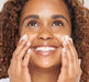 a woman smiling rubbing in her moisturizer 