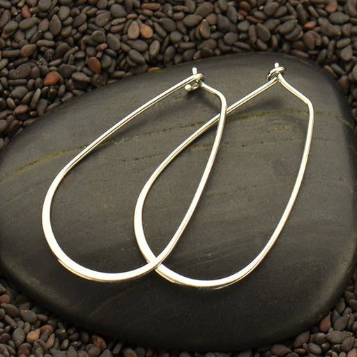a pair of silver hoop earrings sitting on top of a rock