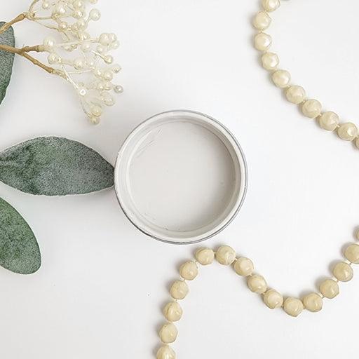a white beaded necklace next to a white cup