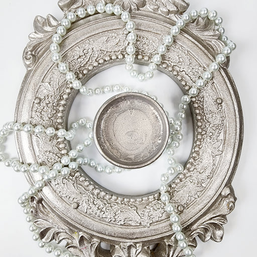 a silver plate with pearls around it on a white surface