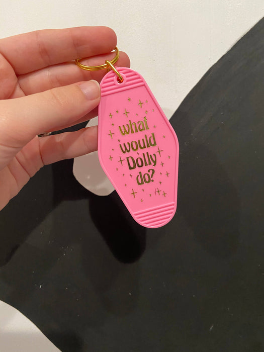 a hand holding a pink keychain that says what would dolly do?