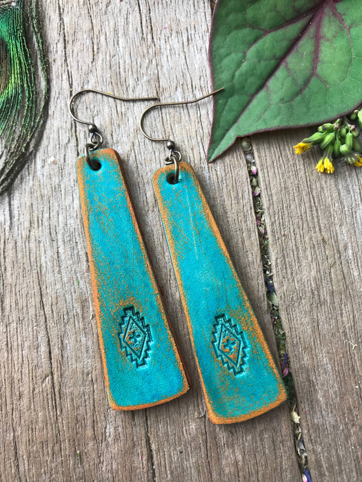 a pair of blue earrings with a green leaf next to it