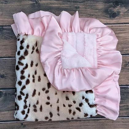 a pink and brown snow leopard print baby blanket on a wooden floor